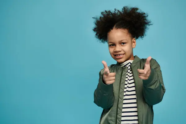 Une jeune afro-américaine aux cheveux bouclés sourit et pointe vers le spectateur dans un décor de studio. — Photo de stock