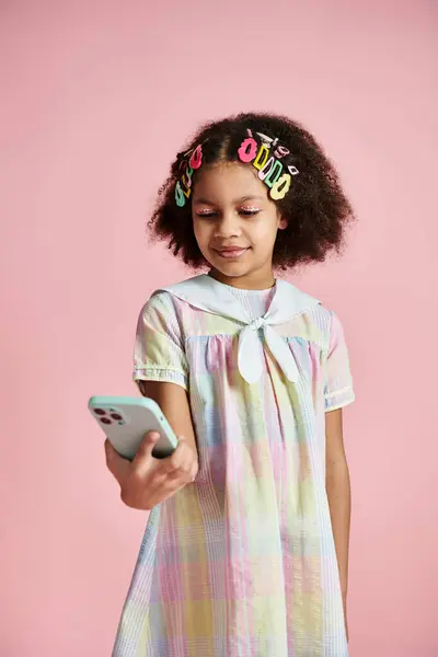 Une jeune afro-américaine avec des pinces à cheveux colorées se tient sur un fond rose tout en utilisant un smartphone. — Photo de stock