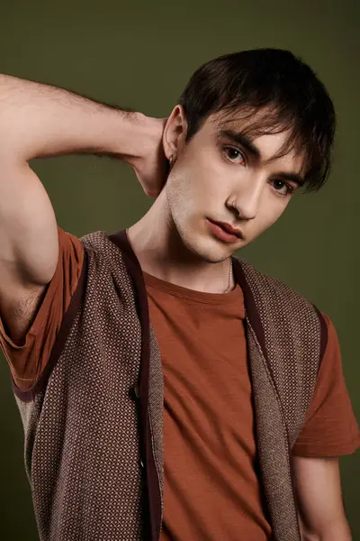 Ein gutaussehender Mann posiert selbstbewusst in brauner Weste und orangefarbenem T-Shirt vor grünem Hintergrund. — Stockfoto