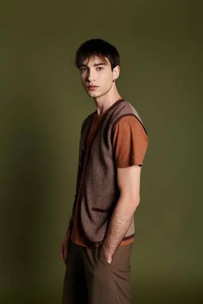 A stylish man wearing a brown vest and brown pants poses against a vibrant green backdrop. — Stock Photo