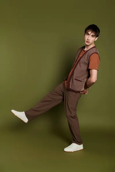 A chic man in brown poses with one leg extended against green. — Stock Photo