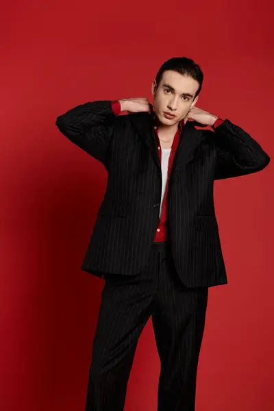 A stylish man in a pinstripe suit poses against a bright red backdrop. — Stock Photo