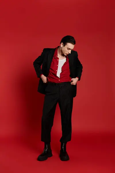 A stylish man in a black suit poses confidently against a vibrant red backdrop. — Stock Photo