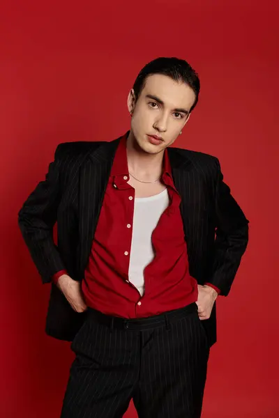 A stylish man in a black pinstripe suit and a red shirt poses against a bold red background. — Stock Photo