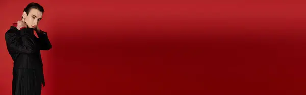 A man in a black suit poses against a red background. — Stock Photo