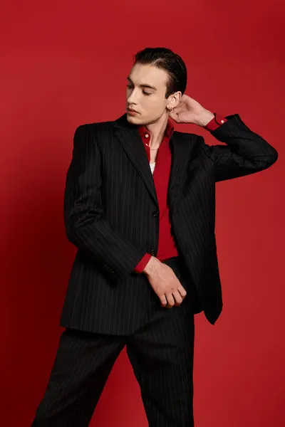 A stylish man wearing a black pinstriped suit stands against a red backdrop. — Stock Photo