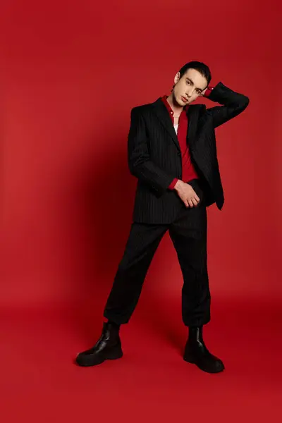 A man in a black suit poses confidently against a red backdrop. — Stock Photo