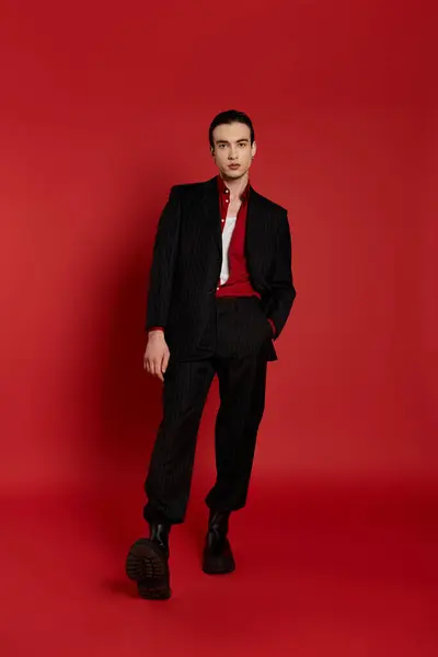 A man in a black suit stands against a red background. — Stock Photo