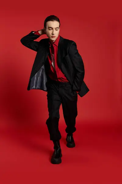 A man in a black suit poses against a vibrant red backdrop. — Stock Photo