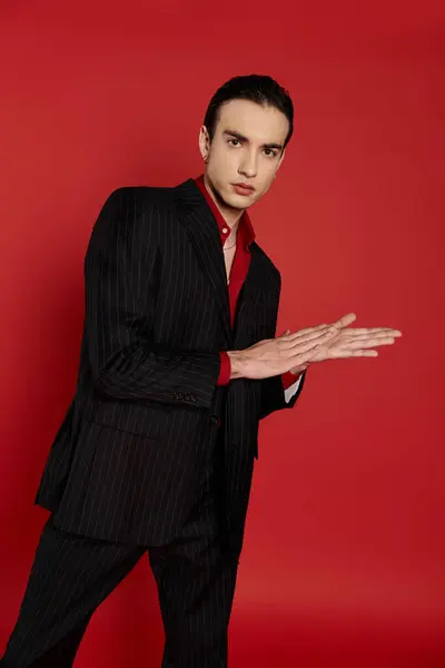 Man in black pinstripe suit poses against bright red backdrop, hand gestures captivatingly. — Stock Photo