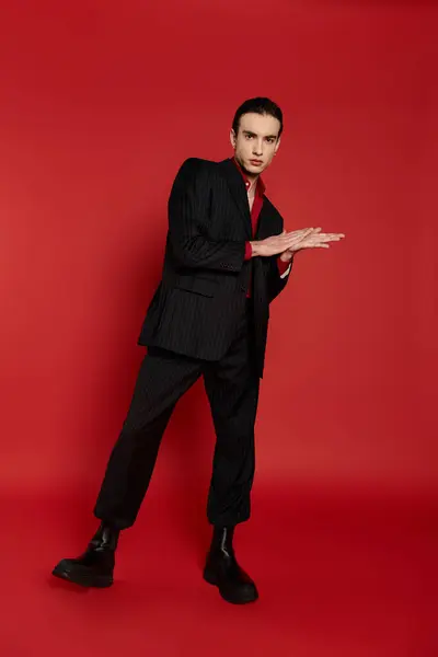 A man in a black suit poses with his hands out in front of him against a bright red background. — Stock Photo