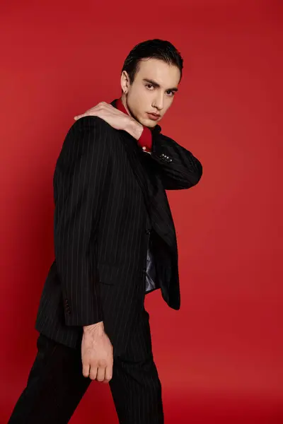 A stylish man in a black suit poses against a red background. — Stock Photo