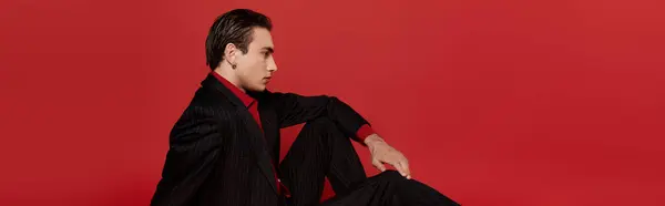 A man in a black suit and red shirt poses against a red background. — Stock Photo