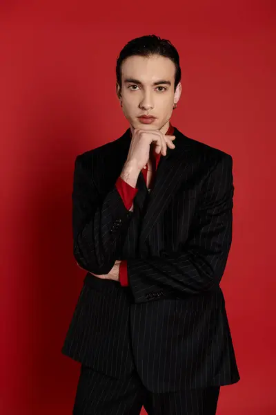 A man wearing a black suit poses with a thoughtful expression against a vibrant red backdrop. — Stock Photo