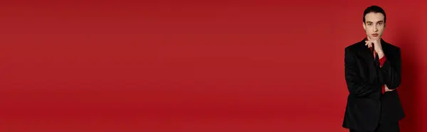 A stylish man in a black suit poses against a bright red backdrop. — Stock Photo