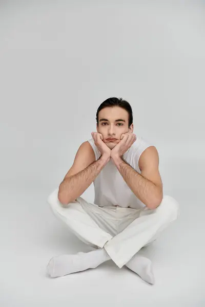 A young man sits cross-legged on a white background, lost in thought. — Stock Photo