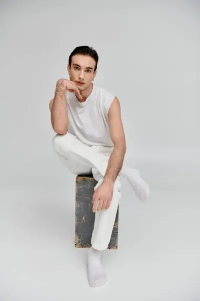A man in white clothing sits thoughtfully on a wooden box against a white backdrop. — Stock Photo