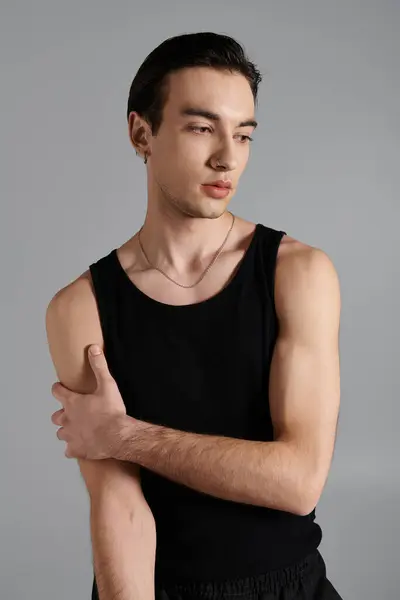 A young man poses against a simple gray background, wearing a black tank top and a gold chain. — Stock Photo