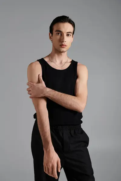 A man in a black tank top and black pants poses against a grey background. — Stock Photo