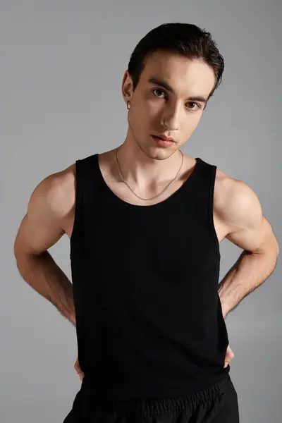 A handsome man in a black tank top poses against a gray backdrop, exuding confidence and style. — Stock Photo