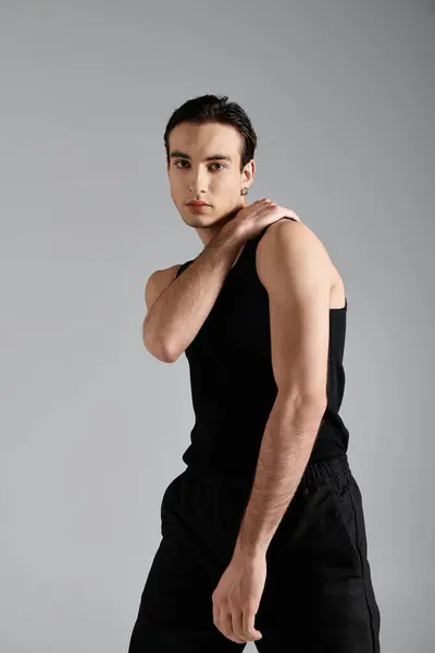 A handsome man in a black tank top poses against a grey background. — Stock Photo