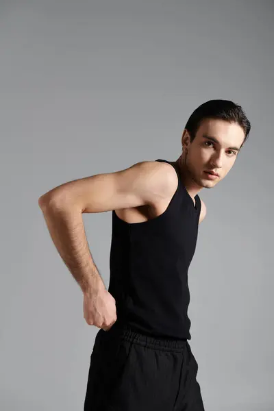 A handsome man in a black tank top and pants poses against a gray backdrop. — Stock Photo