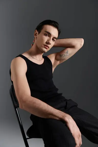 A man in a black tank top poses for a photo, his arm resting on the back of a chair. — Stock Photo