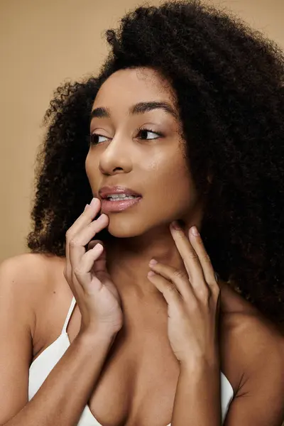 Close-up of a beautiful African American woman with natural makeup, smiling subtly and looking aside against a beige backdrop. — Stock Photo