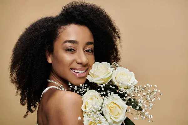 A beautiful African American woman with natural makeup holds a bouquet of white roses against a beige background. — Stock Photo