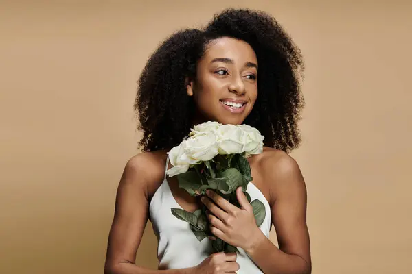 Uma bela mulher afro-americana com maquiagem natural segura um buquê de flores brancas na frente de um fundo bege. — Fotografia de Stock