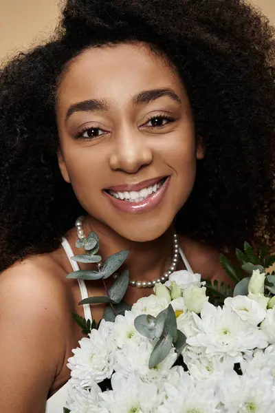 A beautiful African American woman with natural makeup smiles radiantly while holding a bouquet of white flowers. — Stock Photo