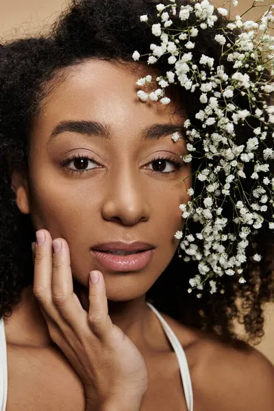 Um retrato de close-up de uma bela mulher afro-americana com maquiagem natural e flores em seu cabelo, posado contra um fundo bege. — Fotografia de Stock