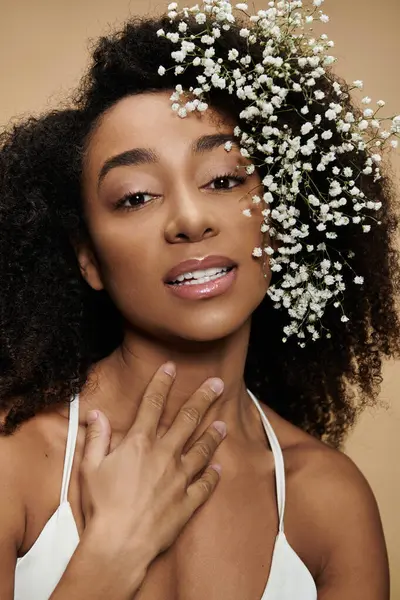 A beautiful African American woman with natural makeup and flowers in her hair smiles softly on a beige background. — Stock Photo
