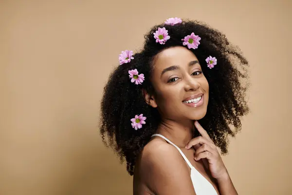 A beautiful African American woman with natural makeup and flowers in her hair smiles against a beige background. — Stock Photo