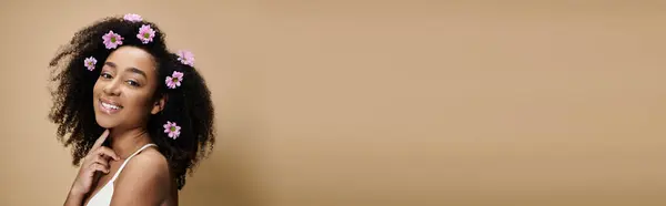 A beautiful African American woman with flowers in her hair smiles radiantly against a beige backdrop. — Stock Photo