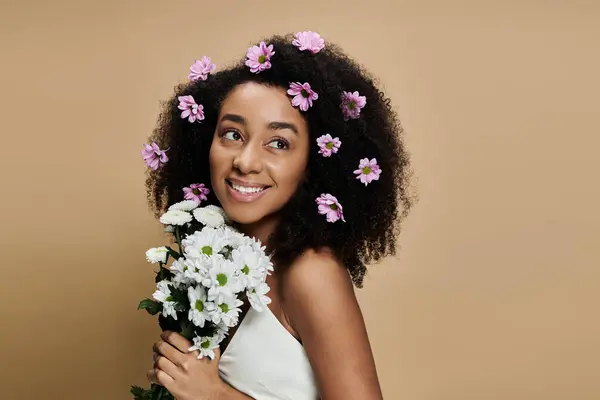 An African American woman with natural makeup smiles and holds a bouquet while wearing pink flowers in her hair. — Stock Photo