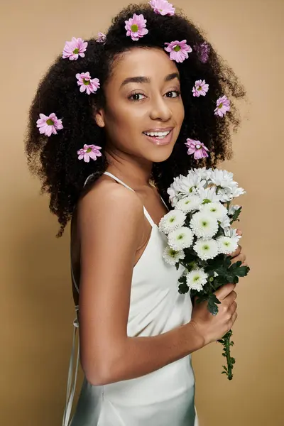 A beautiful African American woman with natural makeup and flowers in her hair smiles while holding a bouquet of white flowers. — Stock Photo