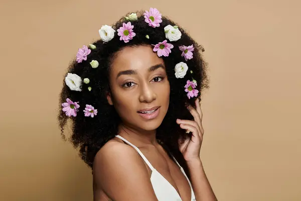A stunning African American woman with natural makeup and flowers in her hair poses against a beige background. — Stock Photo
