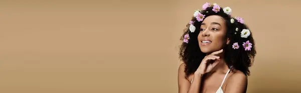A beautiful African American woman with natural makeup and flowers in her hair smiles against a beige background. — Stock Photo