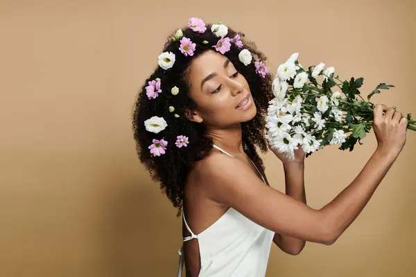An African American woman with natural makeup and flowers in her hair poses against a beige background. — Stock Photo
