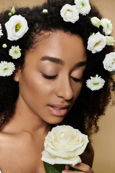 A beautiful African American woman with natural makeup and white flowers in her hair, holding a single white rose. — Stock Photo