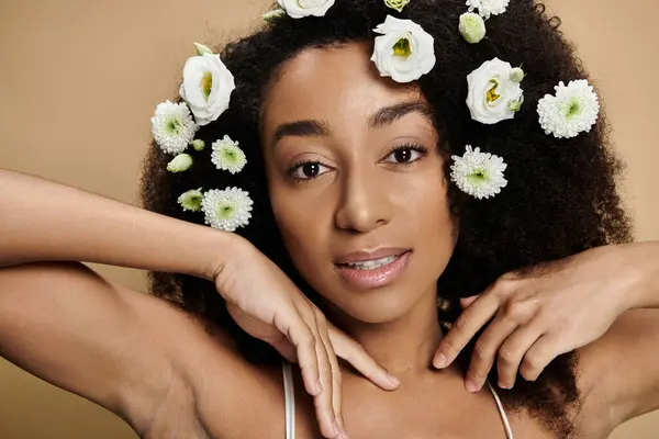 A beautiful African American woman with natural makeup and flowers in her hair poses against a beige background. — Stock Photo