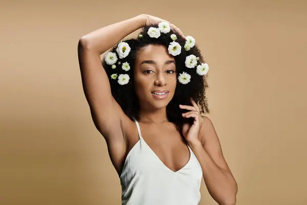 A beautiful African American woman with natural makeup and flowers in her hair smiles softly at the camera against a beige background. — Stock Photo