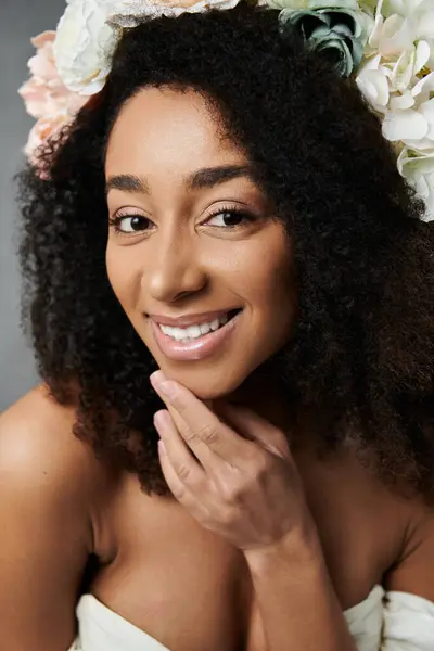 Uma noiva afro-americana bonita em um vestido de noiva branco com flores em seu cabelo sorri suavemente contra um fundo cinza. — Fotografia de Stock