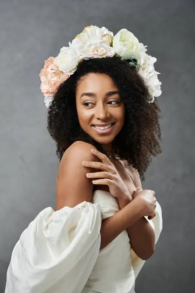 A beautiful African American bride in a white wedding dress smiles and looks over her shoulder, wearing a floral crown. — Stock Photo