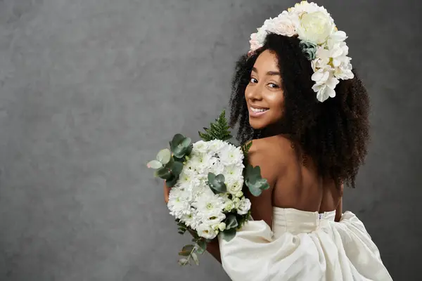 A beautiful African American bride smiles as she poses in a white wedding dress and floral crown against a grey background. — Stock Photo