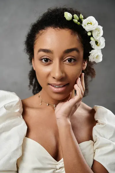 A beautiful African American bride in a white wedding dress with flowers in her hair, posing against a grey background. — Stock Photo