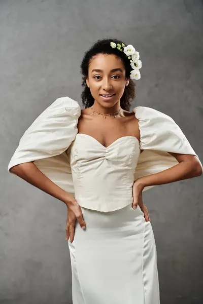 An African American bride in a white wedding dress with floral accents poses against a grey backdrop, radiating elegance and joy. — Stock Photo