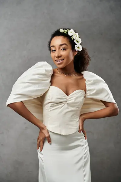 A beautiful African American bride smiles in a white wedding dress with flowers in her hair against a grey background. — Stock Photo