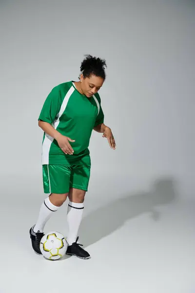 A woman in a green soccer uniform practices her footwork with a soccer ball in a studio setting. — Stock Photo